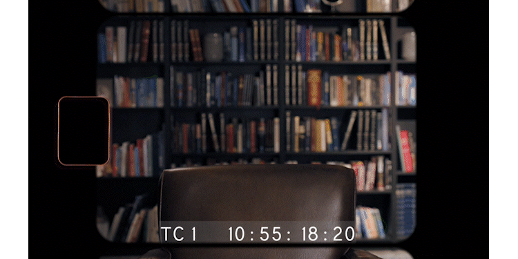 View through a camera or phone screen showing a bookshelf filled with books in a room. The bottom of the screen displays a timestamp of 10:55:18:20.
