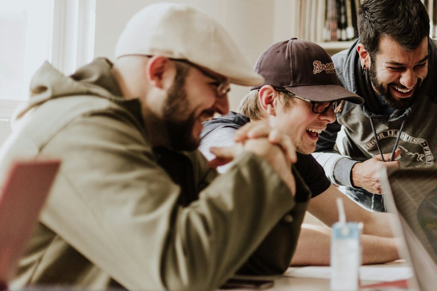 Three young men sitting at a table, laughing and appearing to enjoy a shared moment of fun.
